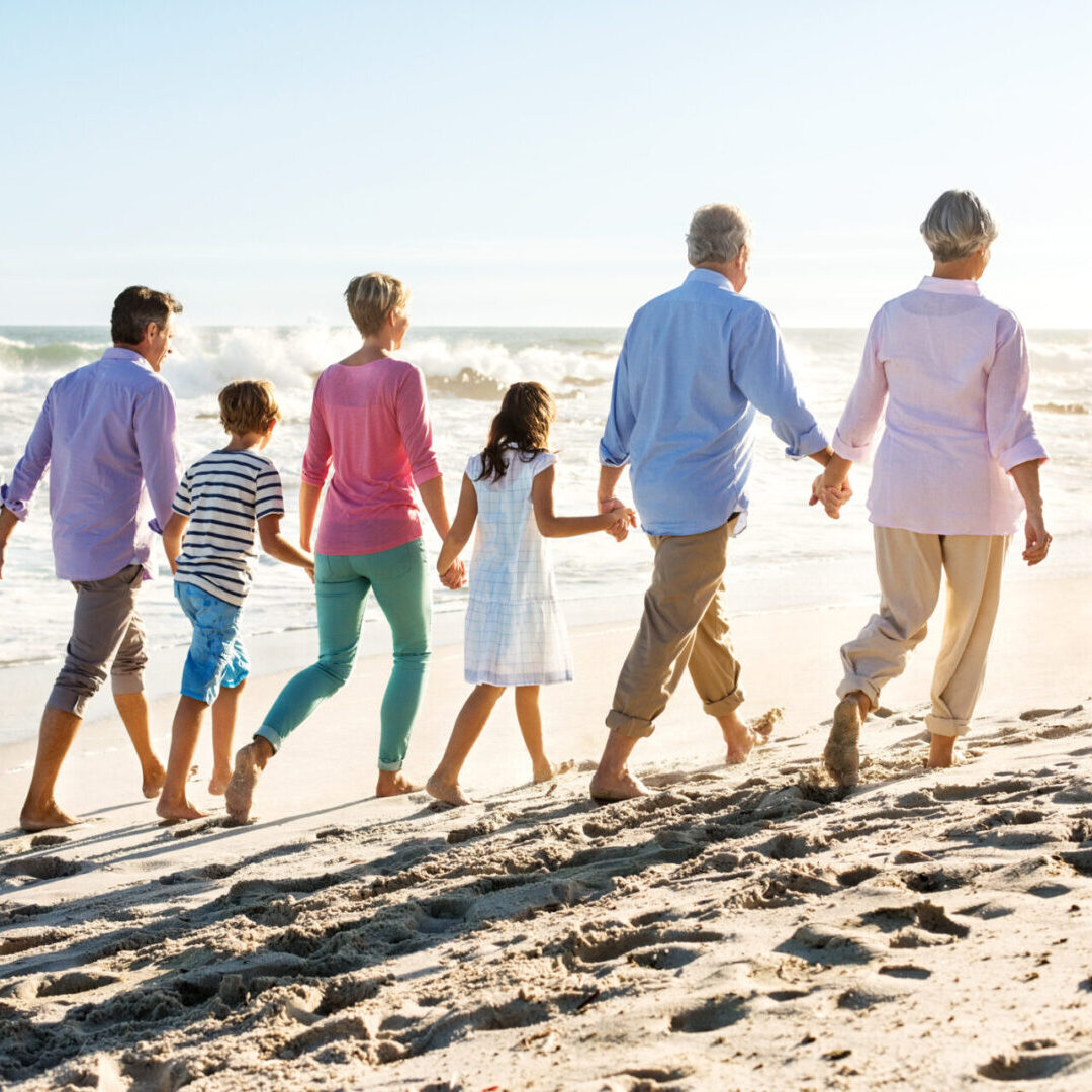 A group of people walking on the beach holding hands.